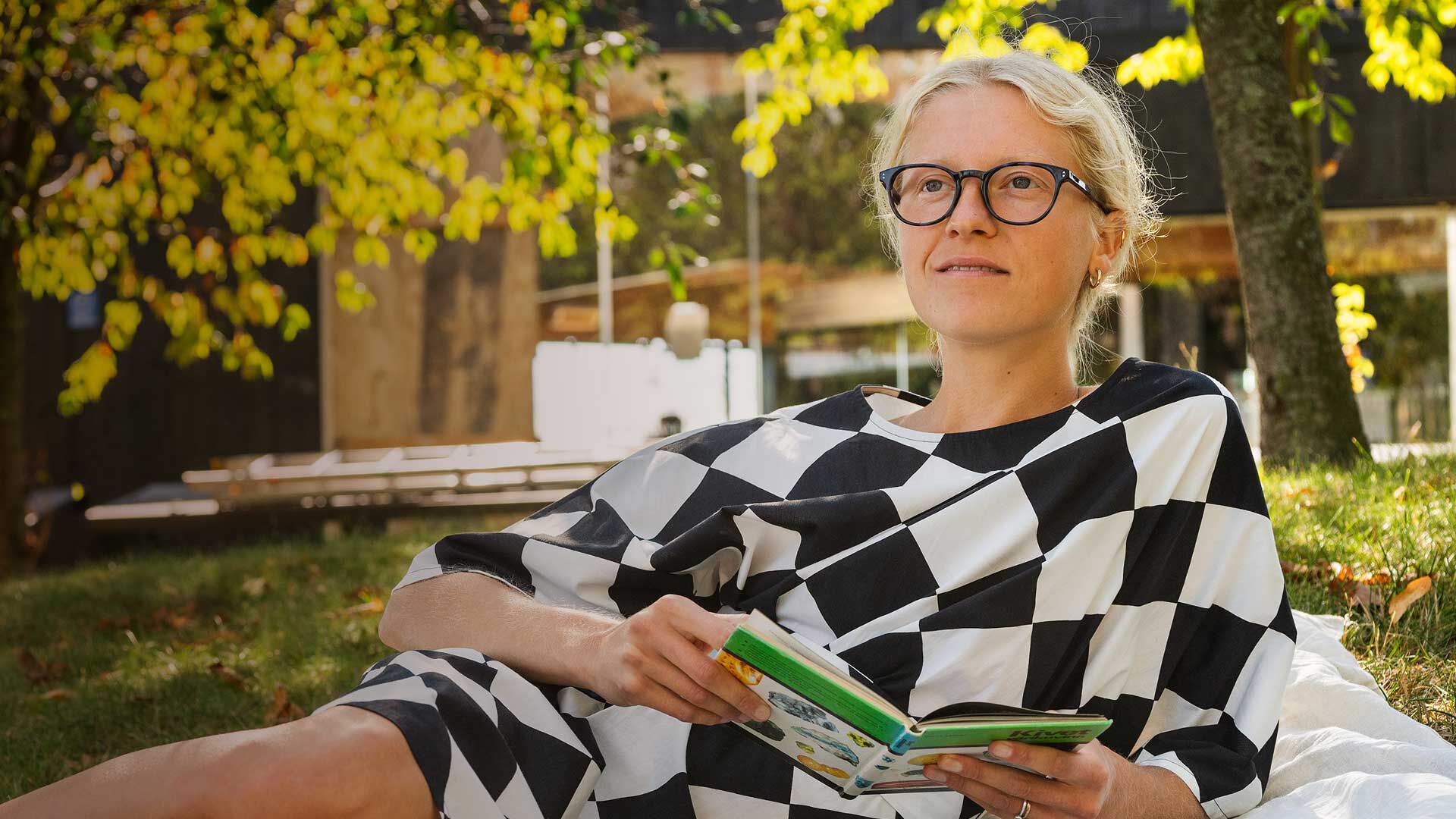 Nainen makaa piknikill&auml;, kirja k&auml;dess&auml;&auml;n